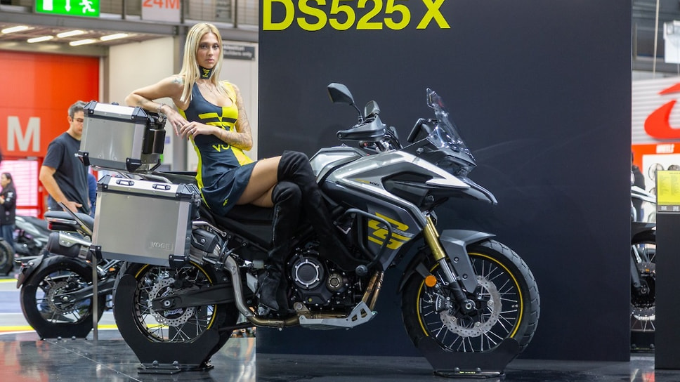 Традиционно рядом с мотоциклами позируют девушки-стендистки. Одна из них — на стенде китайской марки Voge сидит на турэндуро DS525 X