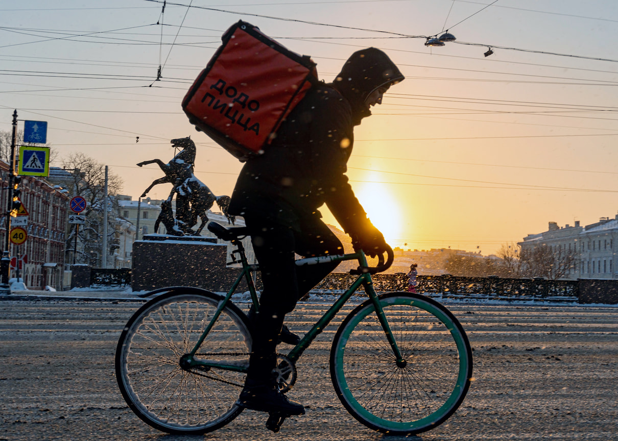 Курьер службы доставки на велосипеде едет по Аничкову мосту в Санкт-Петербурге